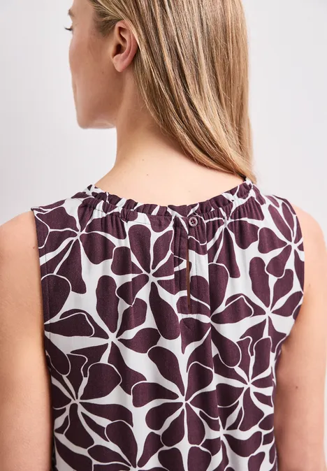 Knielange jurk met ronde halslijn rustic rouge Rugaanzicht van een vrouw met lang blond haar in een mouwloze wijnrode top met lichtblauwe bladprint.