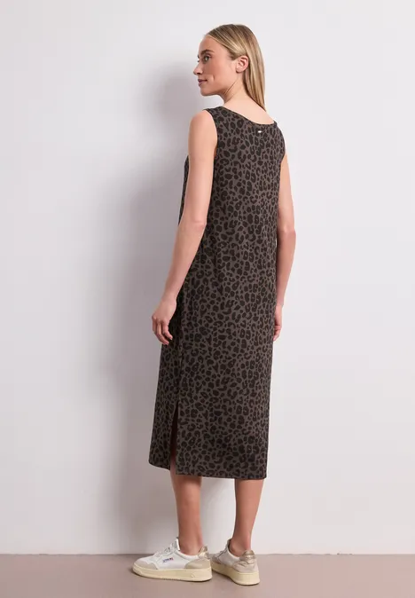 Jersey midi-jurk met leoprint molten earth Vrouw van achteren in een mouwloze midi-jurk met patroon en sneakers voor een witte muur.