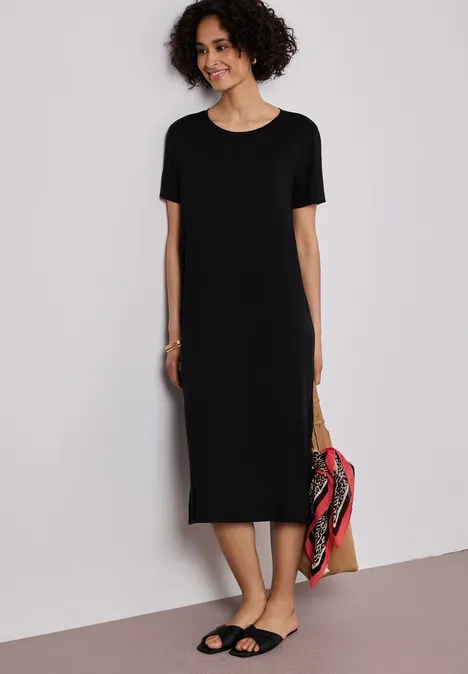 Midi-jurk met korte mouwen en splitdetail Black Vrouw in eenvoudige zwarte midi-jurk met korte mouwen en sandalen, draagt een kleurrijke tas.