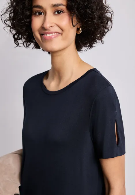 Midi-jurk met korte mouwen en splitdetail shadowed navy Vrouw met krullend haar en creoolse oorbellen draagt zwart kort T-shirt met mouwsplit, gezicht onscherp.