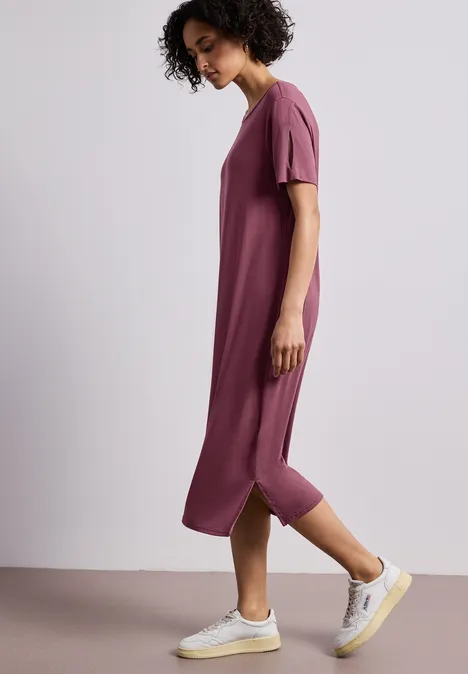 Midi-jurk met korte mouwen en splitdetail dark clouded blush Zijwaarts lopend persoon in losvallende midi-jurk roze-paars en witte sneakers.