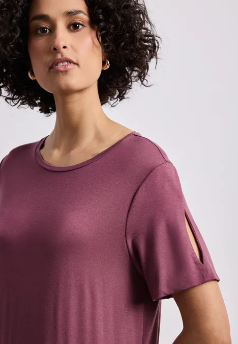 Midi-jurk met korte mouwen en splitdetail dark clouded blush Vrouw met krullend haar draagt een roze t-shirt met korte mouwen en split, kijkt recht in de camera.