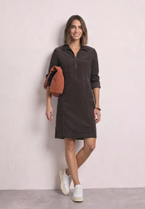 Knielanges Kleid aus Cord mit Zipper black coffee Frau in dunkelbraunem Cordkleid mit halbem Reißverschluss, weißen Sneakern und orangem Clutch.