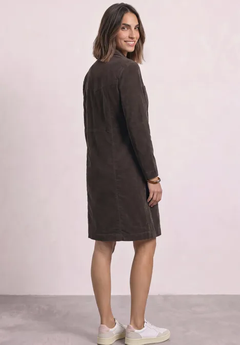 Knielanges Kleid aus Cord mit Zipper black coffee Frau steht seitlich mit Blick über die Schulter, trägt braunes knielanges Kleid und helle Sneaker.