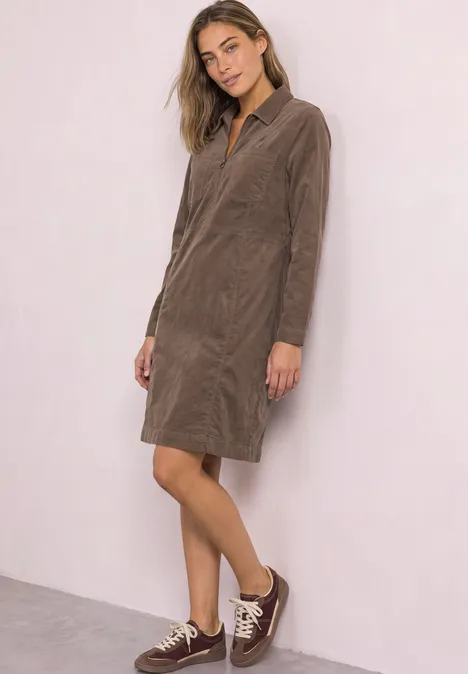 Kniehoge jurk van corduroy met ritssluiting velvet mocha Vrouw draagt een knielange, bruine corduroy overhemdjurk met lange mouwen en bruine sneakers.