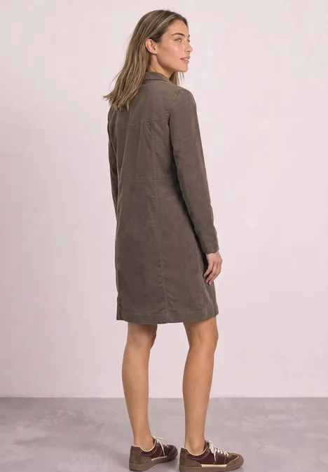Kniehoge jurk van corduroy met ritssluiting velvet mocha Een vrouw staat met de rug naar de camera in een bruine, knielange jas en bruine schoenen tegen een neutrale achtergrond.