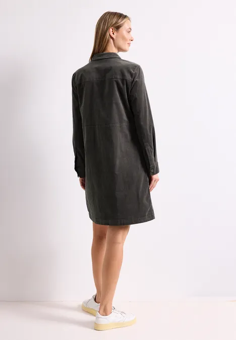 Knielanges Kleid aus softem Cord gravel grey Frau von hinten in dunkelgrauem Hemdkleid und weißen Sneakern vor weißem Hintergrund.