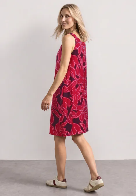 Knielanges Kleid mit gerafften Trägern salsa red Frau in seitlicher Ansicht mit rotem, ärmellosem Kleid mit pinkem Blumenmuster und weißen Schuhen.