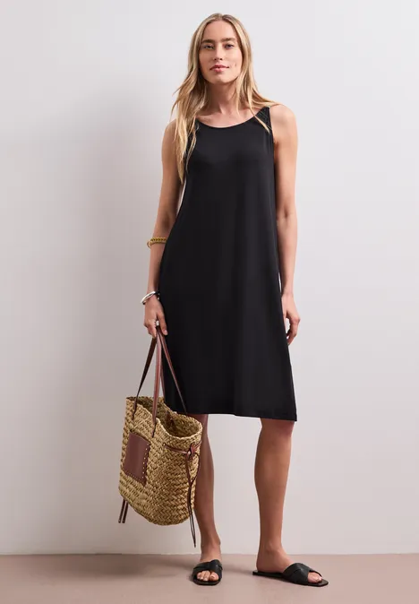 Knielanges Kleid mit Schnallendetail Black Eine Frau trägt ein schwarzes ärmelloses Kleid, hält eine geflochtene Tasche und trägt schwarze Sandalen.