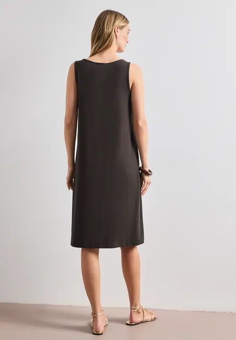 Knielanges Kleid mit Schnallendetail espresso brown Frau von hinten in einem schlichten, ärmellosen knielangen schwarzen Kleid und flachen Sandalen.