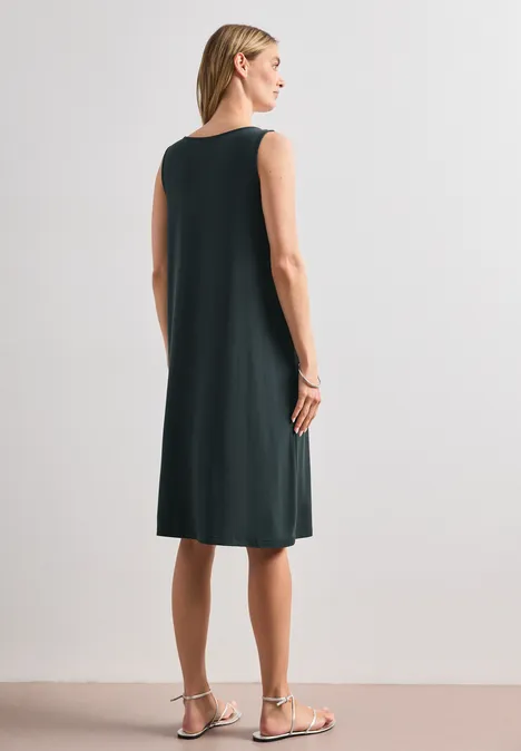Robe longueur genou avec détail de boucle deep bound green Femme de dos dans une robe sans manches mi-longue sombre avec sandales plates sur fond clair
