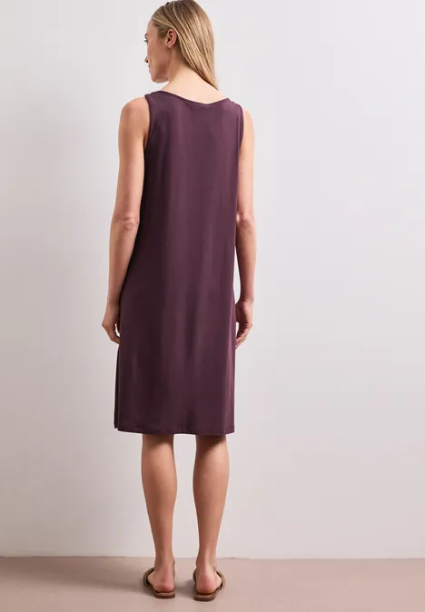 Knielanges Kleid mit Schnallendetail rustic rouge Rückenansicht einer Frau in ärmellosem, knieumspielendem, dunkellila Kleid und flachen Sandalen.