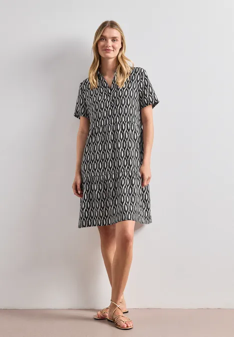 Knielanges Kleid mit Kurzarm und Print clay sand Frau in knielangem, schwarz-weißgemustertem Kleid mit kurzen Ärmeln und Sandalen vor hellem Hintergrund.
