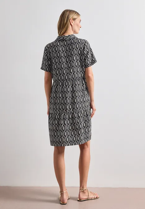 Knielanges Kleid mit Kurzarm und Print clay sand Frau von hinten in knielangem, gemustertem Kleid und Sandalen, vor neutralem Hintergrund.