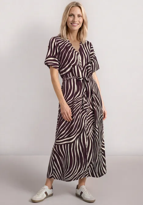 Vrouw in midi-jurk met korte mouwen en wit-bruin streeppatroon, V-hals, gecombineerd met platte sandalen.