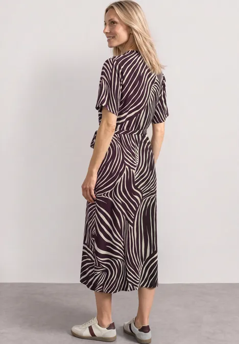 Robe midi avec col en V et imprimé rustic rouge Femme en robe mi-longue à motif zébré, manches courtes et ceinture, sandales plates, fond neutre.