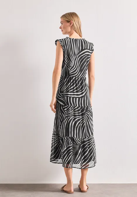 Frau im schwarz-weiß gestreiften Midikleid im Zebramuster, von hinten seitlich vor hellem Hintergrund.