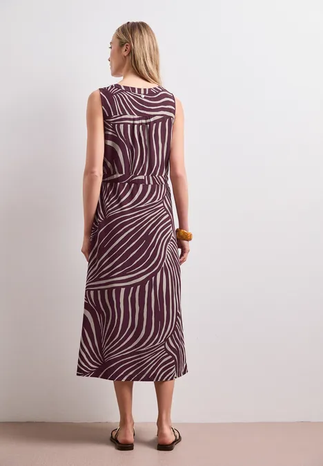 Midi-Kleid mit Split Neck und Zipper rustic rouge Frau von hinten in ärmellosem, midi-langen Kleid mit lila-weißen Zebramuster und flachen Sandalen.