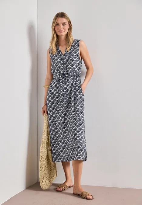 Midi-Kleid mit Split Neck und Zipper shadowed navy Frau trägt ärmelloses, gemustertes Midikleid in Blau-Weiß mit V-Ausschnitt, gebundener Taille, Basttasche und Sandalen.
