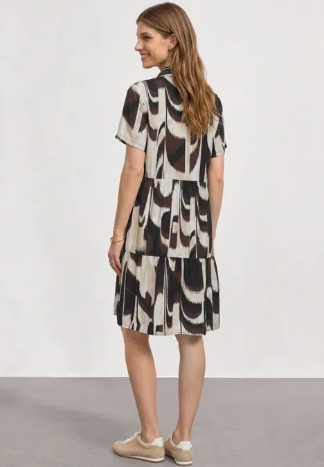 Vrouw van achteren in een losse jurk met zwart-wit geometrisch patroon en comfortabele sneakers.