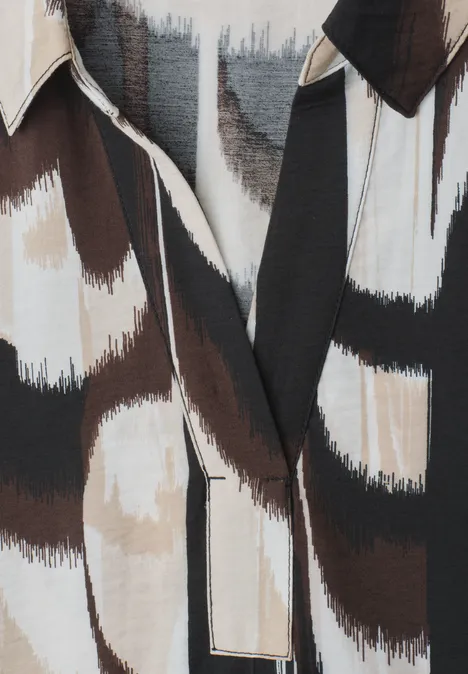 Close-up van een overhemd met abstract penseelstrekenmotief in zwart, bruin en wit.