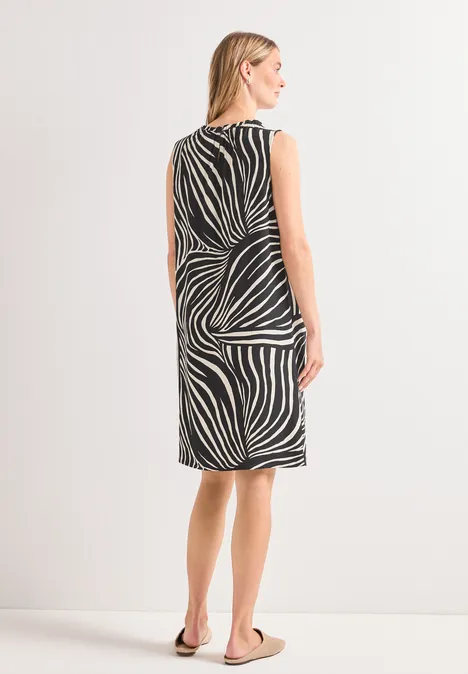 Frau von hinten in knielangem Kleid mit abstraktem schwarz-weiß Print und Sandalen.