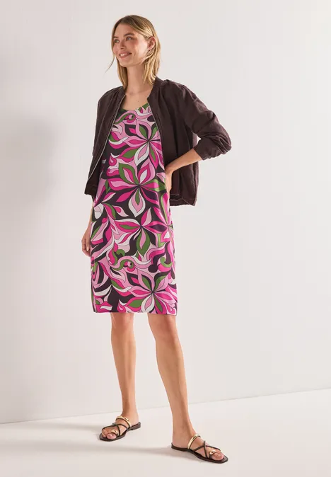 Femme portant une robe droite colorée à motifs floraux, une veste noire et des sandales.