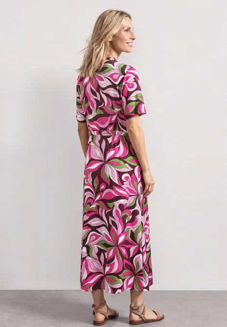 Een persoon draagt een kleurrijke, gebloemde maxi-jurk met sandalen en staat van achteren.