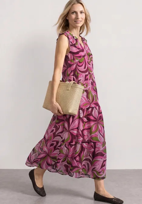 Maxi-Kleid aus Chiffon mit Print magenta dream Frau in geblümtem Maxikleid trägt Korbtasche und schwarze Schuhe im Vorbeigehen.
