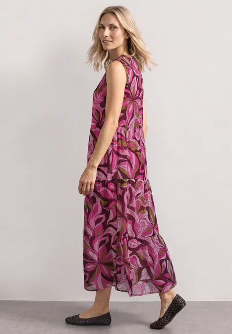 Maxi-Kleid aus Chiffon mit Print magenta dream Frau im seitlichen Profil trägt langes ärmelloses Maxikleid mit pink-lila Blumenmuster und flachen Schuhen.