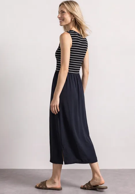 Femme de profil portant un haut sans manches rayé, un pantalon jupe large noir et des sandales marron.