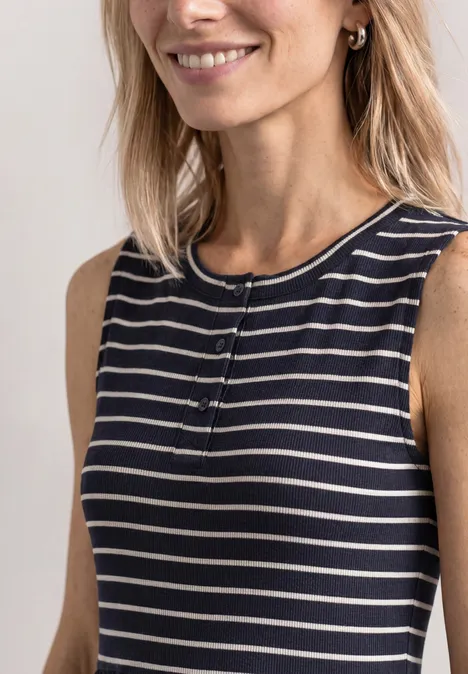 Femme blonde souriante portant un haut sans manches rayé bleu marine et blanc.