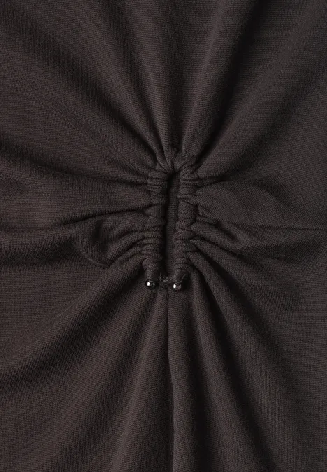 Gros plan sur un tissu sombre froncé au centre, resserré par un cordon terminé par deux embouts métalliques.