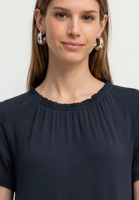 Een vrouw met lang haar draagt een zwart T-shirt en zilveren oorbellen.