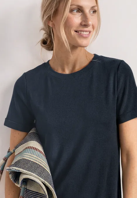 Midikleid in Rippstruktur mit Rundhals darkest blue Frau mit dunkelblauem T-Shirt, seitliche Pose, hält gemusterten Stoff unter dem Arm.