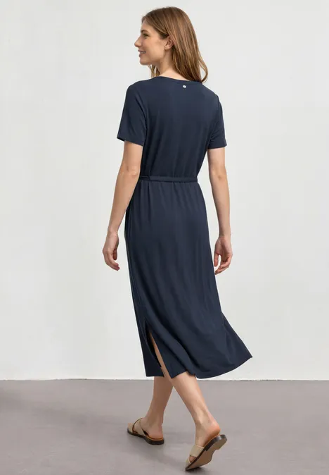 Frau von hinten in knöchellangem, marineblauen Kleid mit kurzem Ärmel, seitlichem Schlitz und Sandalen.