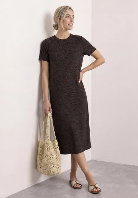 Midi-jurk met grafisch patroon molten earth Vrouw in zwarte T-shirtjurk met kleine stippen, platte sandalen en een gehaakte tas.