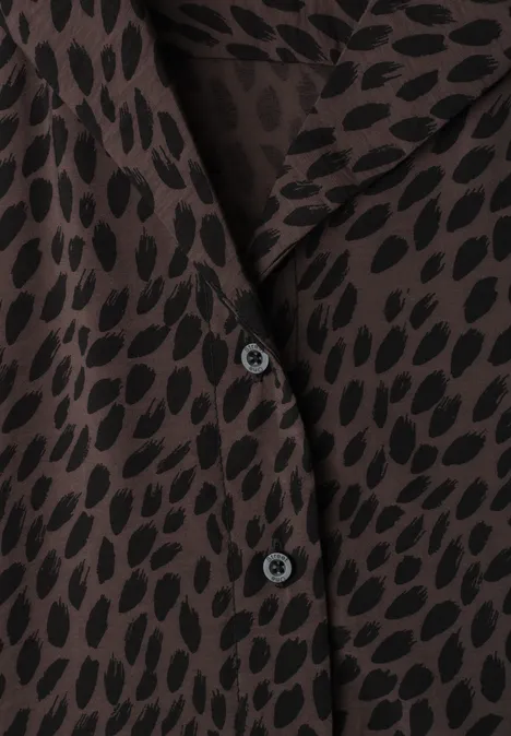 Close-up van een bruin overhemd met zwart patroon en zwarte knopen.