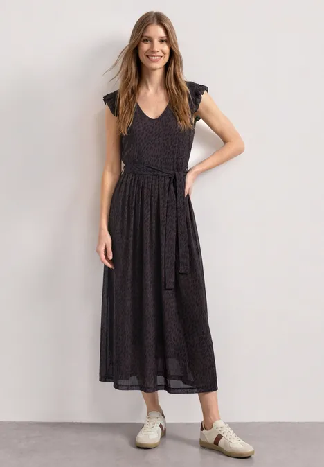 Midikleid aus Mesh mit Print rustic rouge Frau in schwarzem, kurzärmeligem Midikleid mit Gürtel und weißen Sneakern, steht vor hellem Hintergrund.