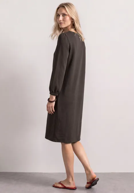 Femme portant une robe mi-longue ample gris foncé à manches longues et des sandales rouges.