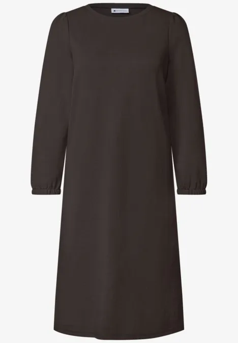 Une robe droite brun foncé, manches longues, encolure ronde et poignets élastiques, longueur genoux.