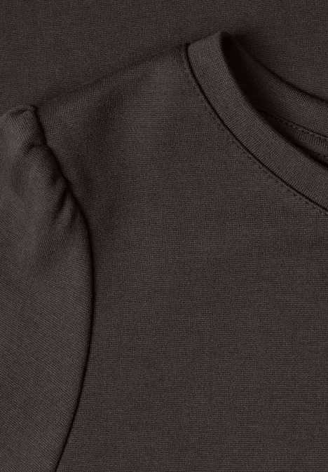 Gros plan de l'encolure d'un t-shirt marron foncé avec un détail plissé sur l'épaule.