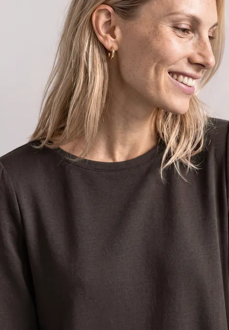 Portrait d'une femme souriante aux cheveux blonds, portant des boucles d'oreilles dorées et un haut noir.