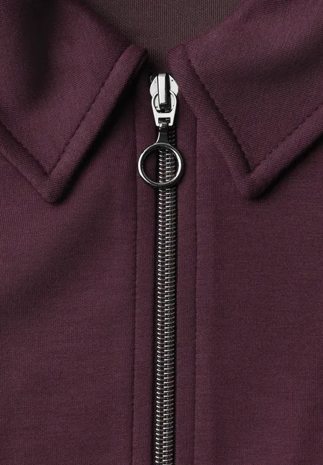 Robe en molleton arrivant aux genoux, avec fermeture éclair rustic rouge Gros plan d’un vêtement bordeaux avec une fermeture éclair centrale au curseur rond.