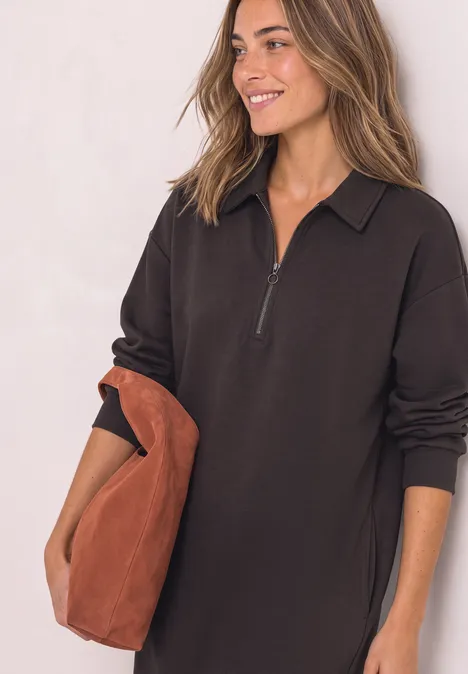 Robe en molleton arrivant aux genoux, avec fermeture éclair black coffee Femme en robe noire à manches longues zippée, souriante, tenant un grand sac marron.