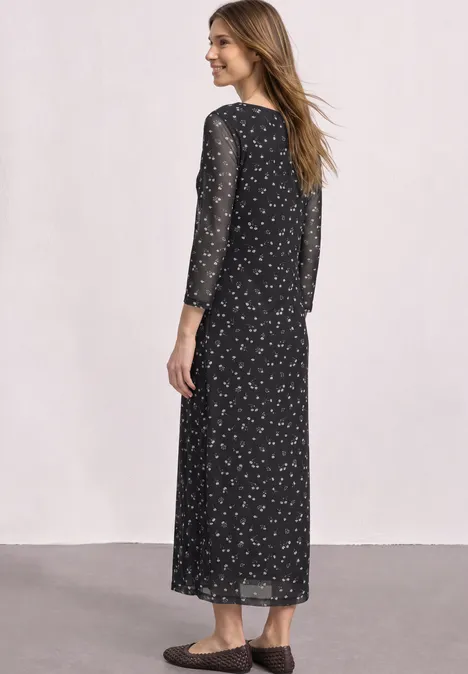 Frau in langem schwarzem Kleid mit kleinem Blumenmuster, von hinten gesehen