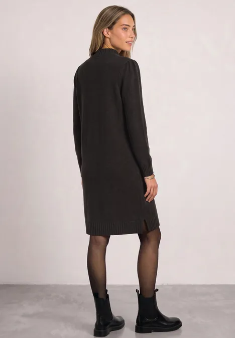 Frau in schwarzem Strickkleid mit langen Ärmeln, blickt über die Schulter, dazu schwarze Boots und feine Strumpfhose.