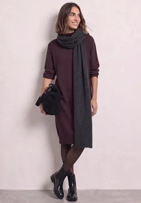 Frau trägt bordeauxfarbenes Kleid, langen dunkelgrauen Schal, schwarze Boots und Handtasche.