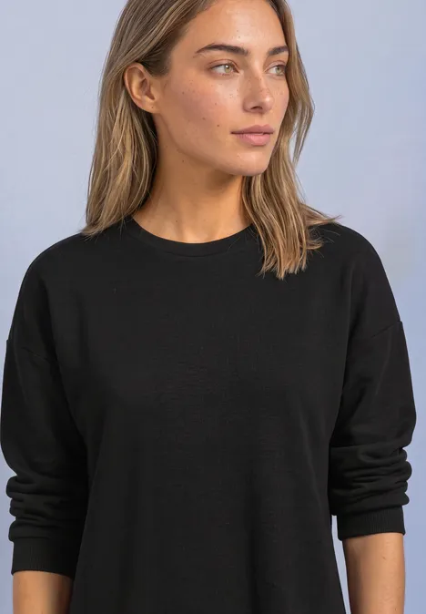 Knielanges Sweatkleid mit Spitzenkante Black Frau trägt schlichten schwarzen Pullover, blickt zur Seite, vor neutralem Hintergrund.