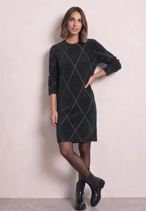 Robe à carreaux arrivant aux genoux armor grey Femme portant une robe pull grise à losanges, collants noirs et bottines, posant devant un fond clair